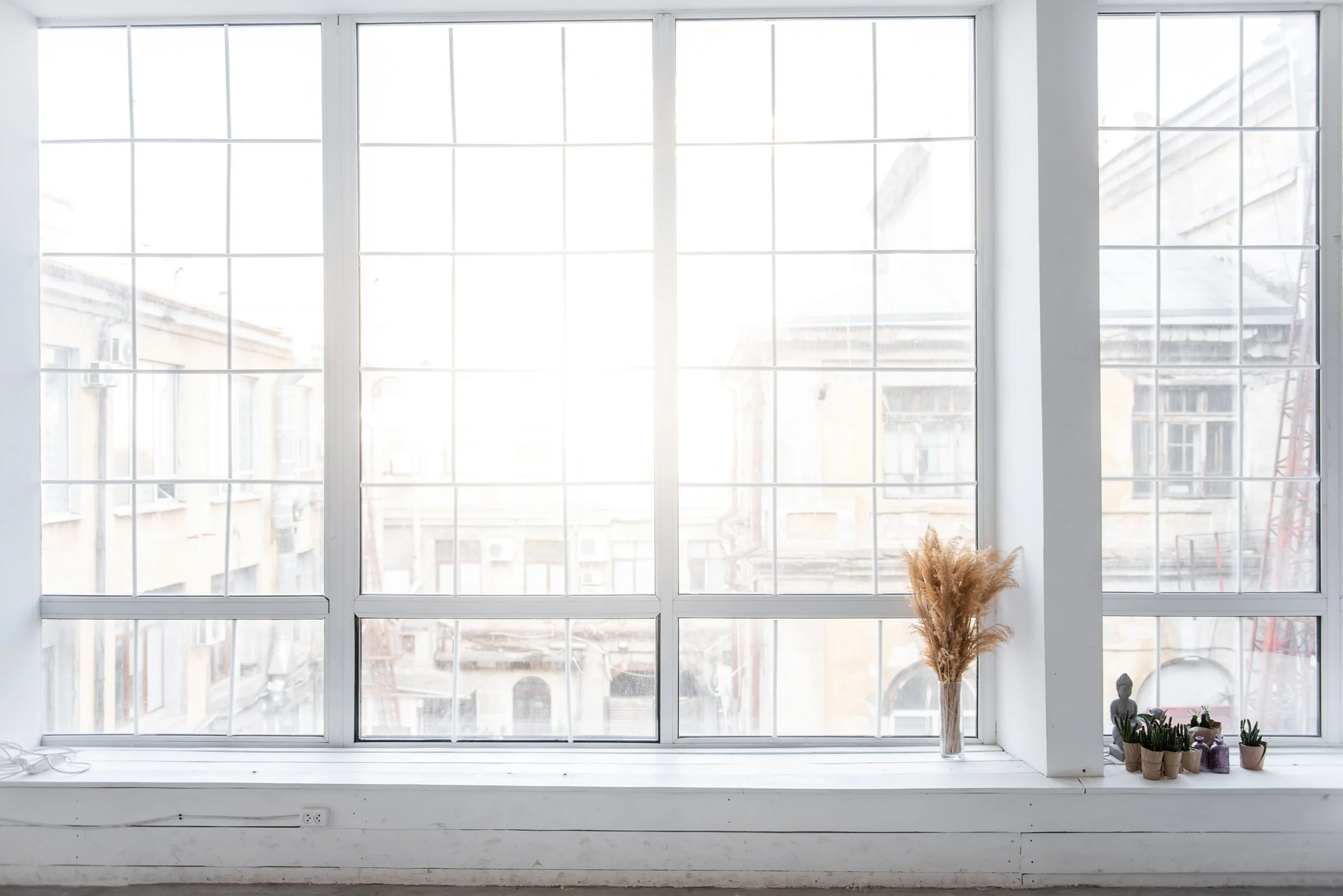Glass vase with pampas grass dried reeds stands by large panoramic window on white wooden windowsill