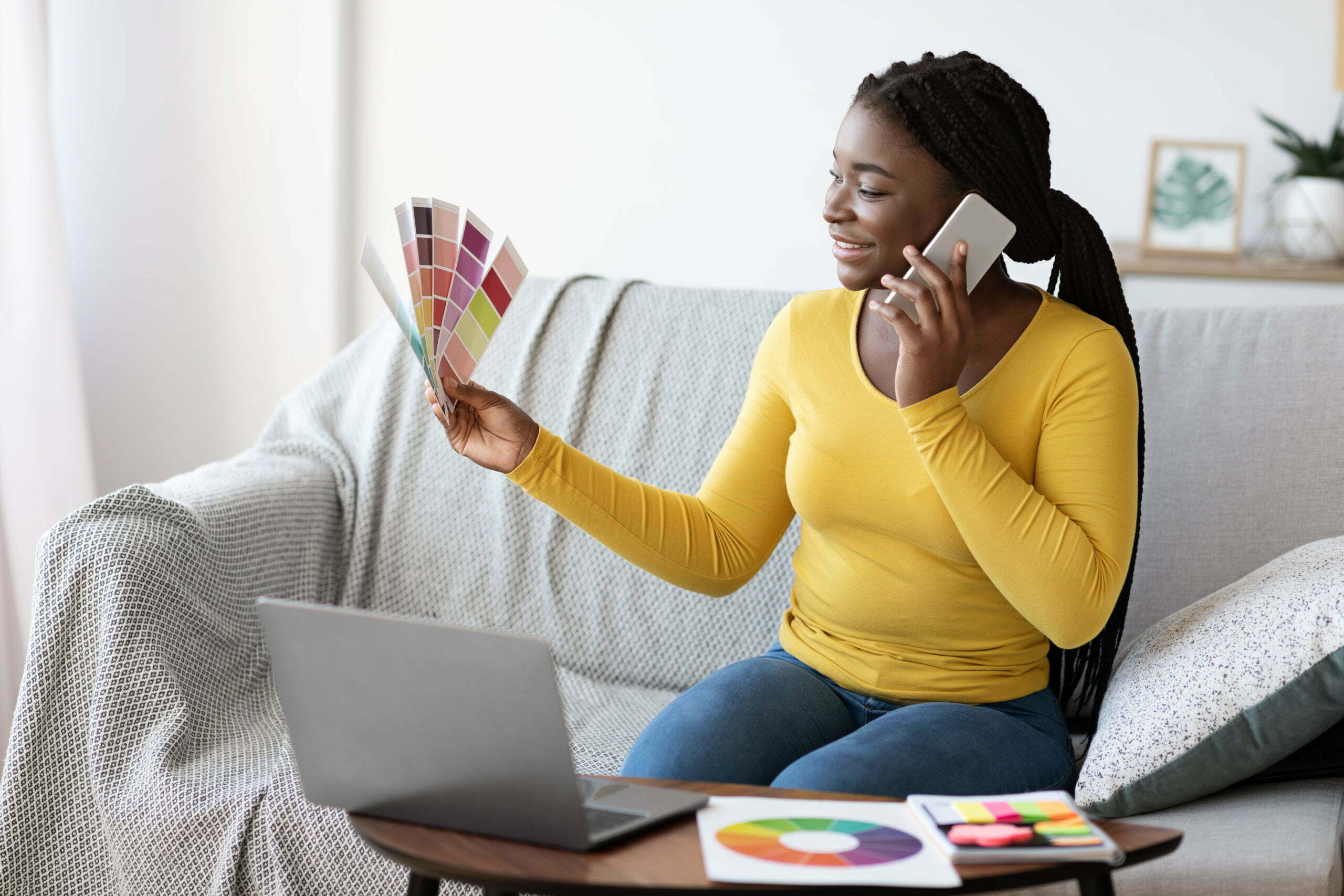 Young Black Lady Holding Color Swatch And Talking On Cellphone At Home
